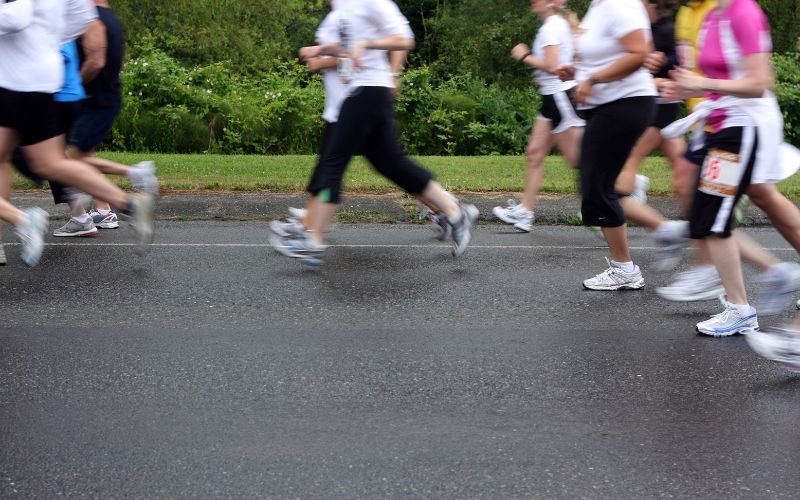 Zdjęcie przedstawia kobiety biegnące po asfaltowej drodze
