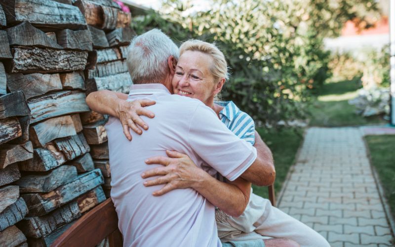 Zdjęcie przedstawia parę emerytów, którzy się przytulają na ławce