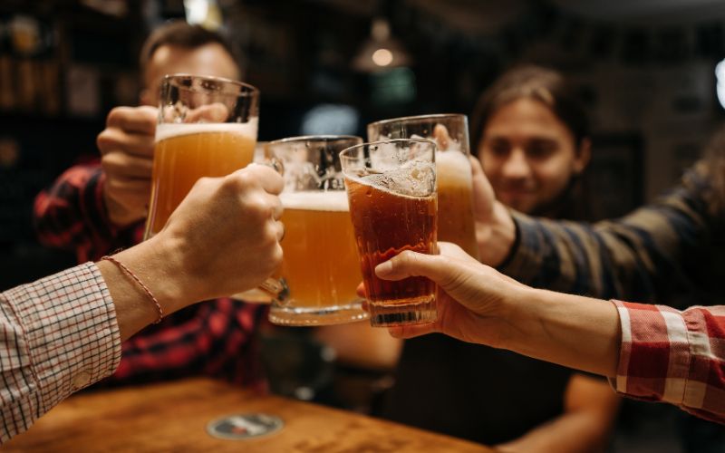 Zdjęcie przedstawia znajomych, którzy stukają się kuflami w pubie
