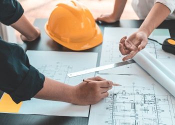 Inżynierowie omawiają projekty budowlane przy żółtym kasku.